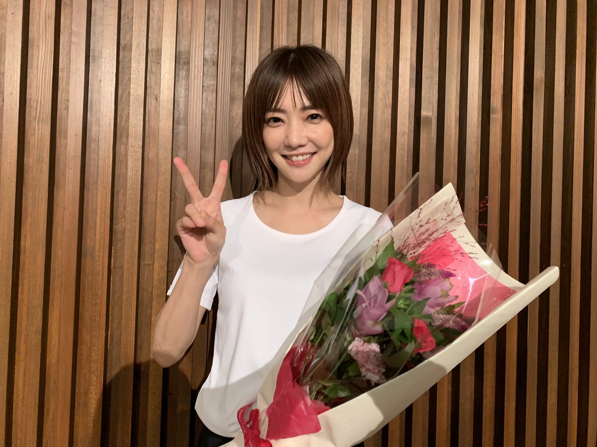 笑顔の倉科カナが右手でピースして左手で花束を持っている