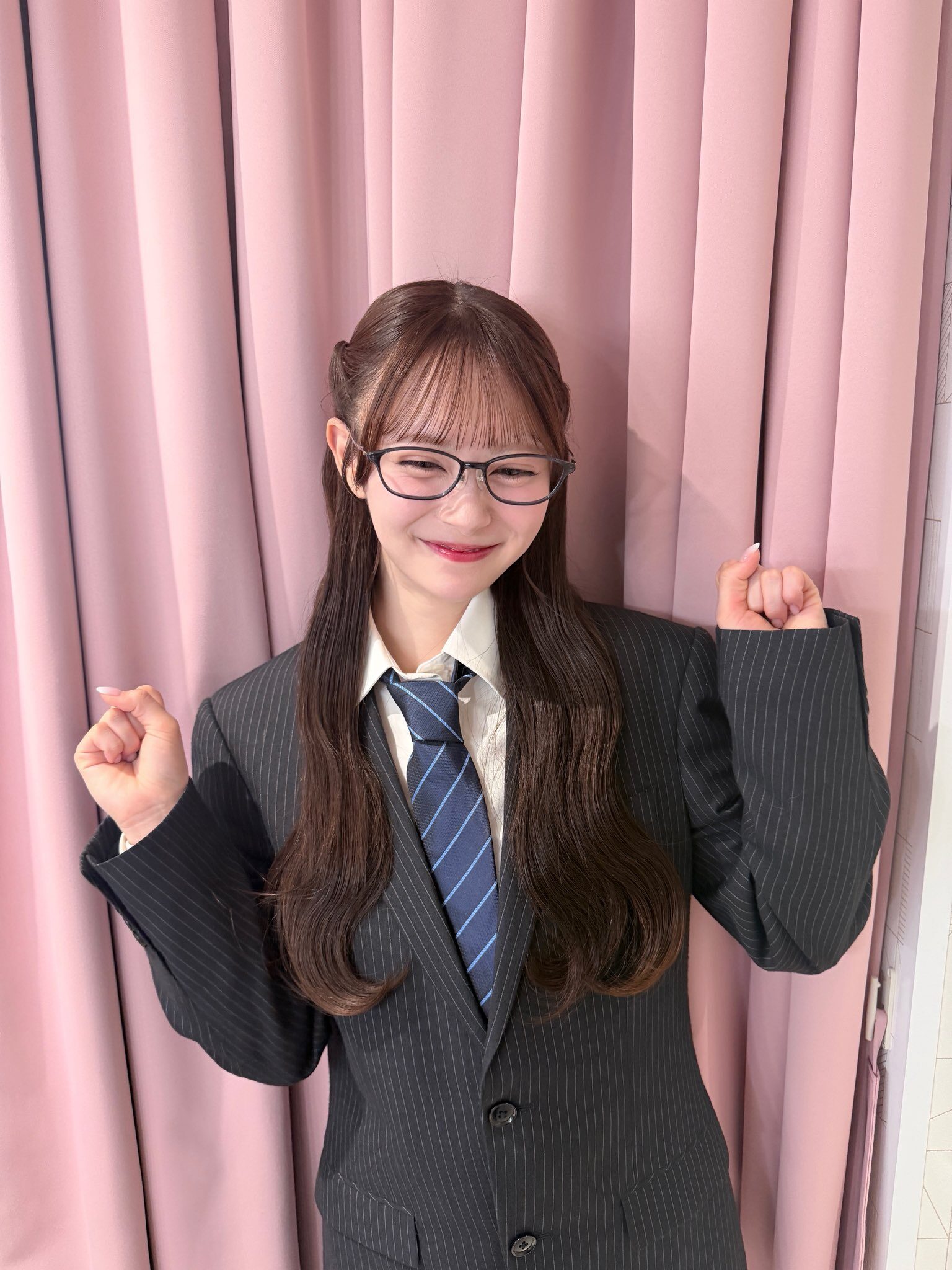 メガネ、スーツ姿の笑顔の伊藤百花が両肘を曲げて両腕を挙げている