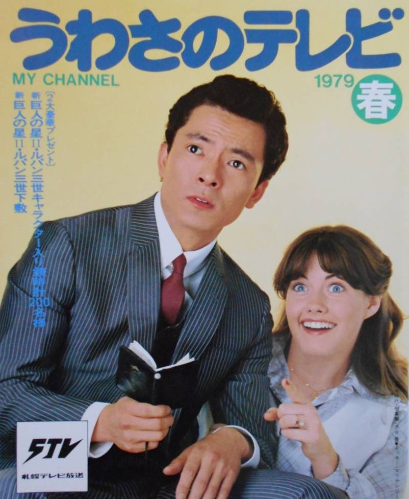 水谷豊が右手で手帳を持ち、笑顔のミッキー・マッケンジーが左手で前を指差している