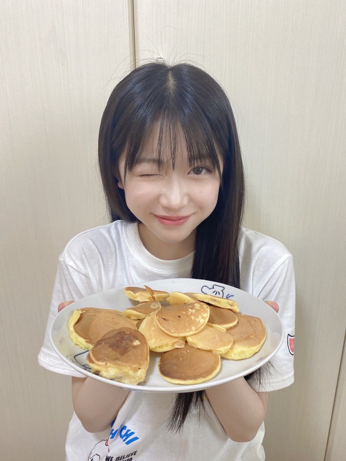 五藤希愛がウインクして大皿にのったミニパンケーキ数個を見せている