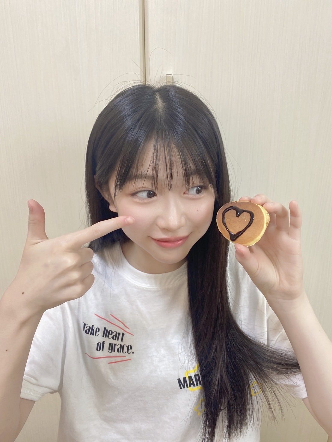 五藤希愛がミニパンケーキを左手で持って、右手で指さしている。目線はミニパンケーキ